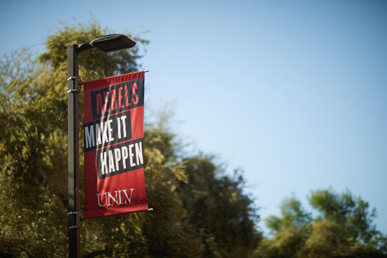 A UNLV banner that reads &quot;Rebels make it happen&quot; hangs from a light pole.