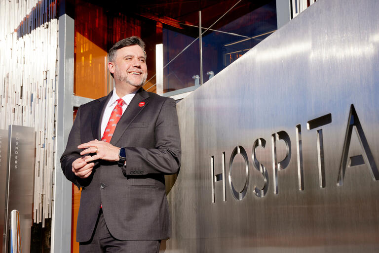 man in suit leaning against silver wall that reads hospitality