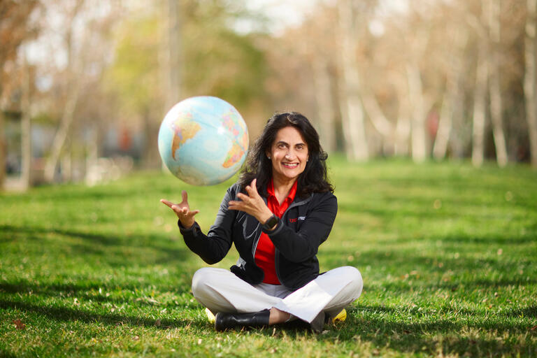 Rimi Marwah sitting on the grass cross-legged and throwing a globe into the air