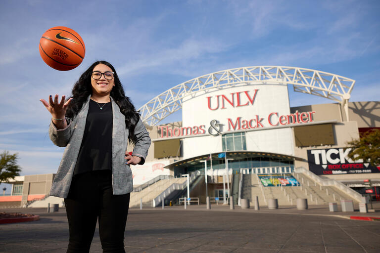 woman throws basketball in air while standing in front of Thomas &amp; Mack Center
