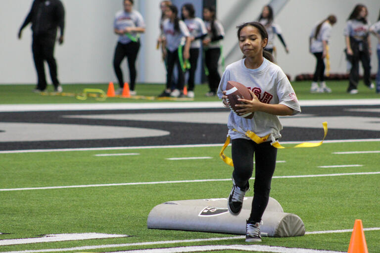 young female student carrying football across field